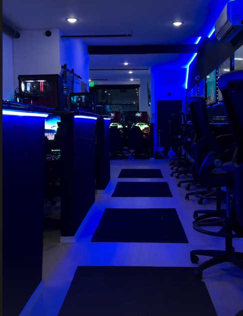 Blue-lit interior of Open World Gaming Center with gaming chairs and mats leading to stations