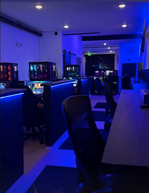 Rows of gaming PCs with RGB towers under blue LED lighting inside Open World Gaming Center